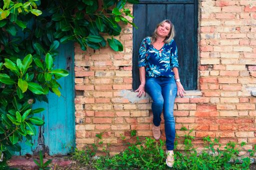 Woman leaning against a window of an old house. Brick facade and leaves around. Aratuipe, Bahia.