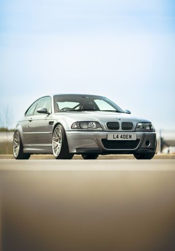 A vertical shot of grey modern BMW M3 CSL on the road with blue sky in the background