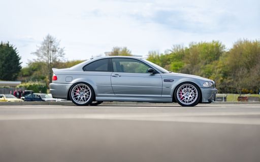 A grey modern BMW M3 CSL on the road surrounded by green trees