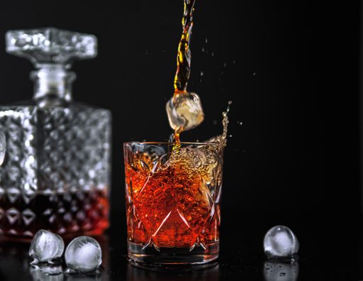 A closeup of a crystal glass of whiskey and a splash from falling ice on a black background