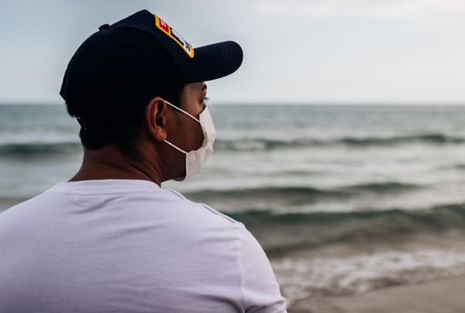 A closeup portrait of a young Hispanic man wearing a medical mask on the beach