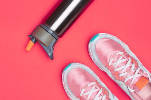 A top view of  stylish and fashionable sneakers and water bottle on the red surface