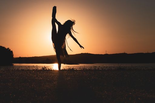 The silhouette of a ballerina posing by a lake - concept: freedom, elegance