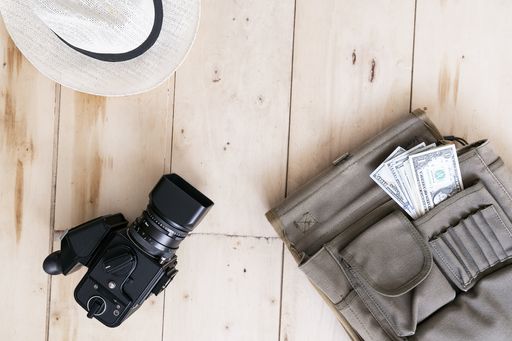 A top view of a backpack with money, a camera, and a hat on the wooden surface- travel concept