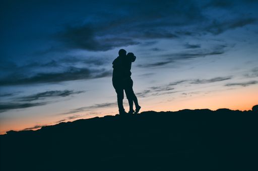 A silhouette of a kissing couple in nature at sunset
