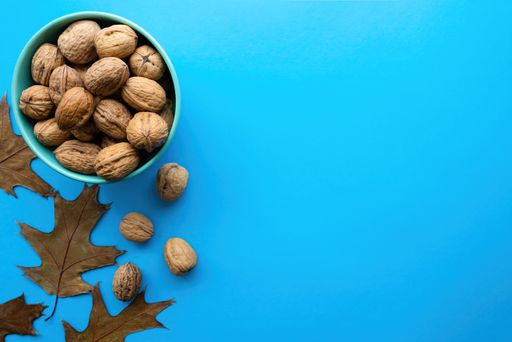 A closeup shot of a bowl of walnuts with dry autumn leaves on a blue background