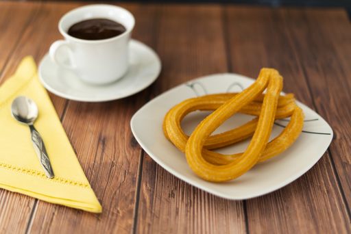 A closeup shot of a cup of hot chocolate with churros on the table