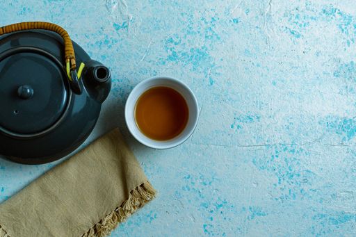 A top view of a gray teapot and a cup on blue background