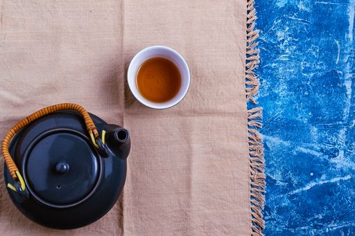 A top view of a teapot and a cup on brown fabric and blue background