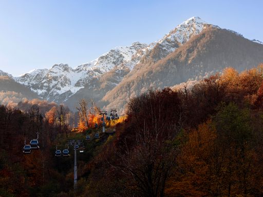 An aerial view of cable cars over an autumn landscape with snowy mountain peaks in the background in Sochi, Russia
