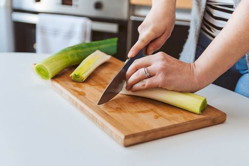 A closeup shot of a woman cutting leek onions on a wooden board in the kitchen