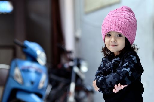 A cute little South Asian girl in a pink hat with crossed arms
