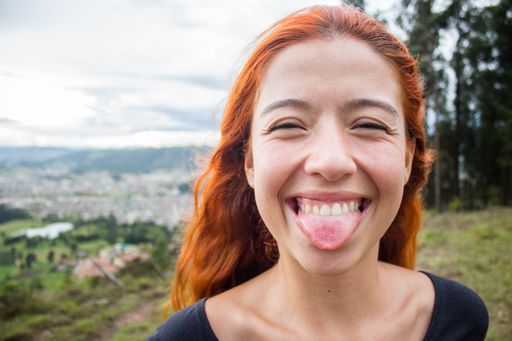 A shallow focus of a cheerful female with ginger hair sticking her tongue out in a field