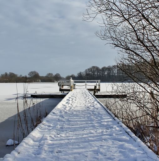 A wooden dock covered in the snow over a frozen lake in winter
