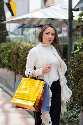 A vertical portrait of an attractive elegant woman walking in the city streets with shopping bags