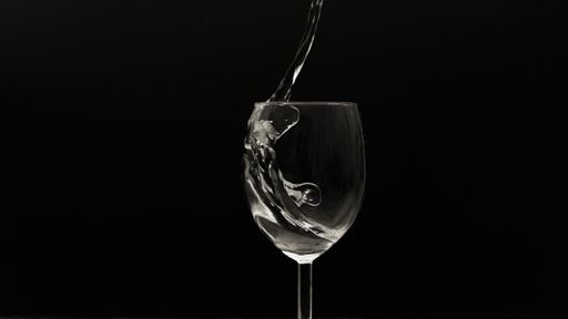 Wine glass on a pitch-black background with liquid pouring in it from above