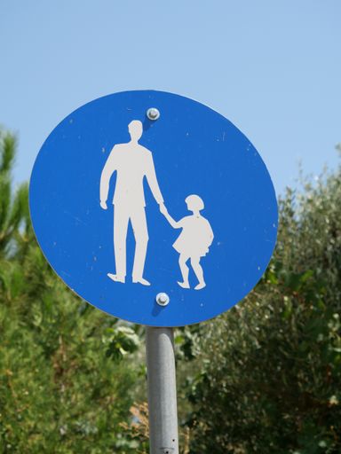 A vertical shot of a blue round road sign indicating pedestrians walking with kids