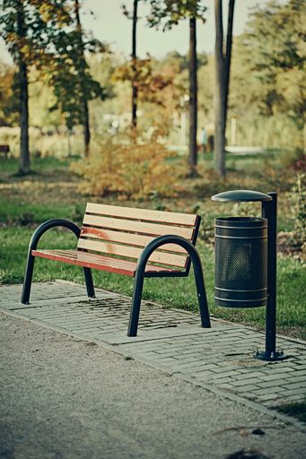 A vertical shot of a wooden bench and a bin in an autumna park
