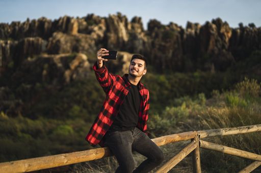 A young man taking a selfie while sitting on a railing at a park