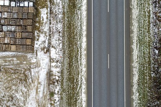 A high angle view of a road surrounded by a meadow covered with the snow with metallic objects on it