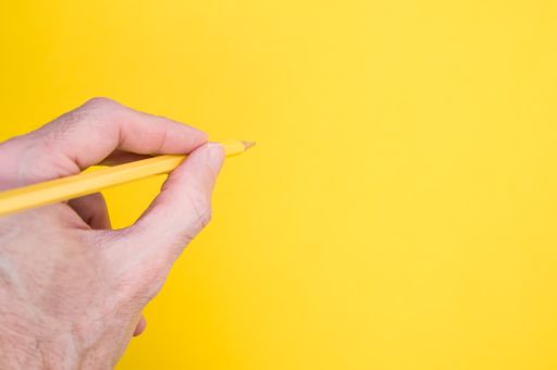 A closeup of a person holding a yellow pencil on the yellow surface - space for text