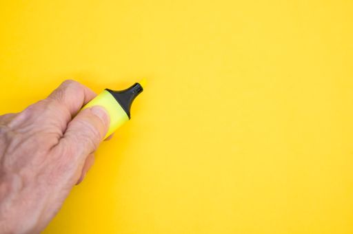 A closeup of a person holding a highlighter pen on the yellow surface - space for text