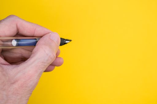 A closeup of a person holding a fountain pen on the yellow surface - space for text
