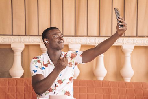 Ethnic black guy taking a piece of fruit from the bowl and enjoying music on cell phone while taking a selfie