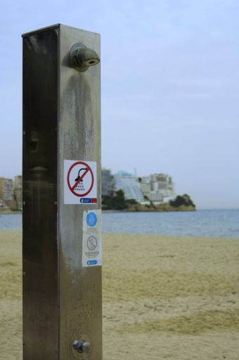 A vertical shot of a water shower at the beach with a ''no shower'' sign