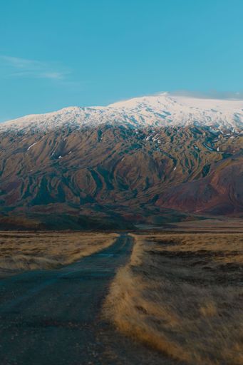 A lonely road leading to snowy mountains under the blue sky in Iceland