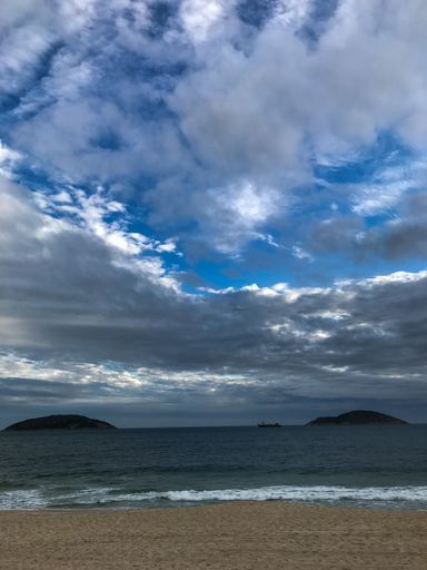 A vertical shot of a wavy sea and sandy beach under cloudy sky