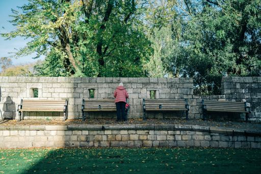 An old lady standing in front of wooden benches in the park on a sunny day