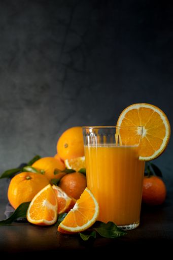Low key light image of a glass of fresh orange juice next to a set of oranges and tangerines ready to squeeze