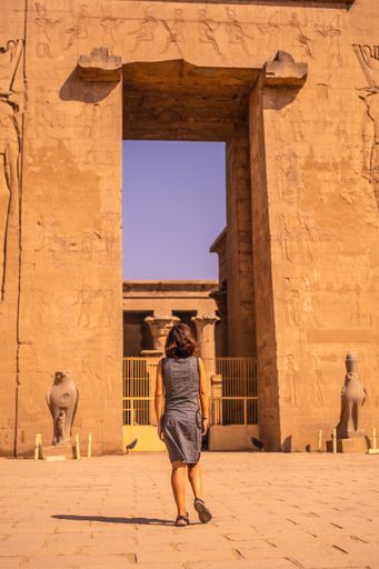 A vertical shot of a young female wearing a dress and walking around The Temple of Horus at Edfu, Egypt