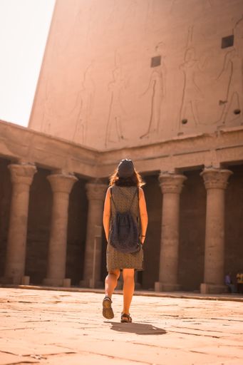 A vertical shot of a young female wearing a dress and walking around The Temple of Horus at Edfu, Egypt