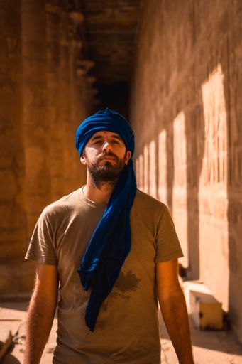 A vertical shot of a Caucasian man with a scarf on his head in The Temple of Horus at Edfu, Egypt