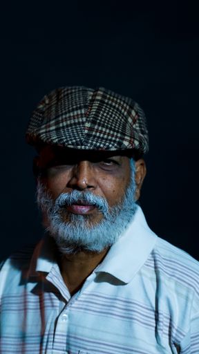 A vertical shot of an Asian middle-aged man with a beard hat and a serious face