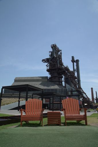 a vertical shot of two red wooden seats near a gray building with a tower under a clear sky