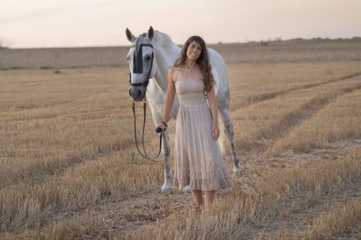An attractive young Caucasian female with a beautiful dress riding a horse in the countryside