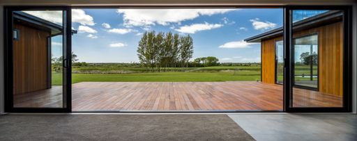 A view from a modern house with big glass doors looking at the green field