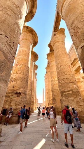 Vertical shot of tourists walking around ancient columns with Egyptian carvings in Karnak Temple in old Luxor city