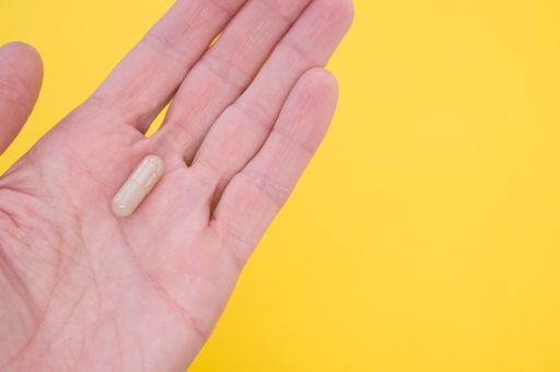 A capsule on a hand palm on yellow background with a copy space