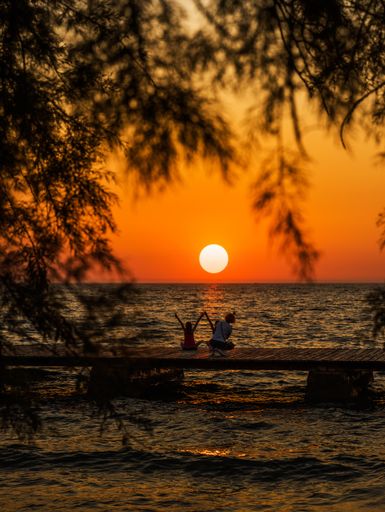 A mother taking a photo of her children sitting on the beach with the beautiful view of the sunset
