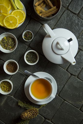 A vertical high angle shot of a cup of tea, a teapot, tea leaves, cinnamon and orange slices on the table