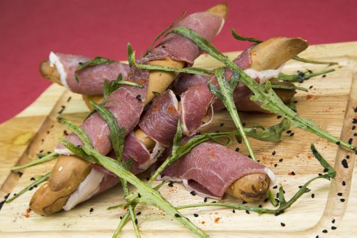 A closeup shot of grissini breadsticks with prosciutto ham on a chopping board