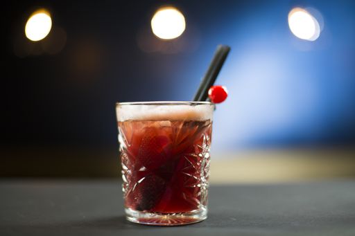 A closeup shot of an alcoholic drink in a glass cup with cherry on the table