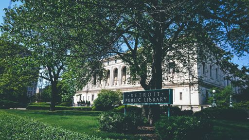 The Detroit Public Library in a park surrounded by greenery under a blue sky and sunlight
