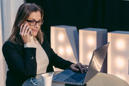 An adult gorgeous woman having a smartphone conversation while sitting in front of open laptop computer in a cafe bar