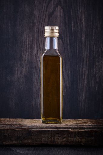 A vertical shot of a transparent bottle filled with olive oil on dark background
