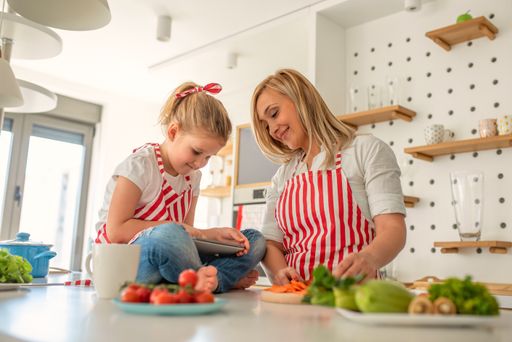 A cute daughter playing on the phone while the mother is cooking